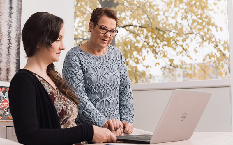 Kaksi naista tarkastelee asiakirjaa kannettavan tietokoneen näytöltä pöydän äärellä.