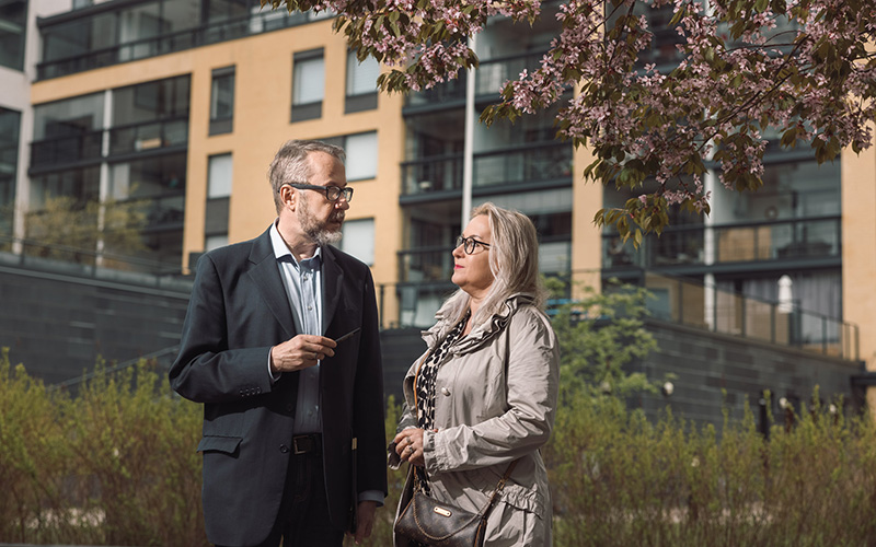 Isännöitsijä ja osakas juttelevat kukkivan kirsikkapuun alla, taustalla näkyy keltainen kerrostalo.